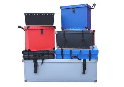 A stack of six metal storage trunks in various colors and sizes, with handles and latches, arranged on a white background.