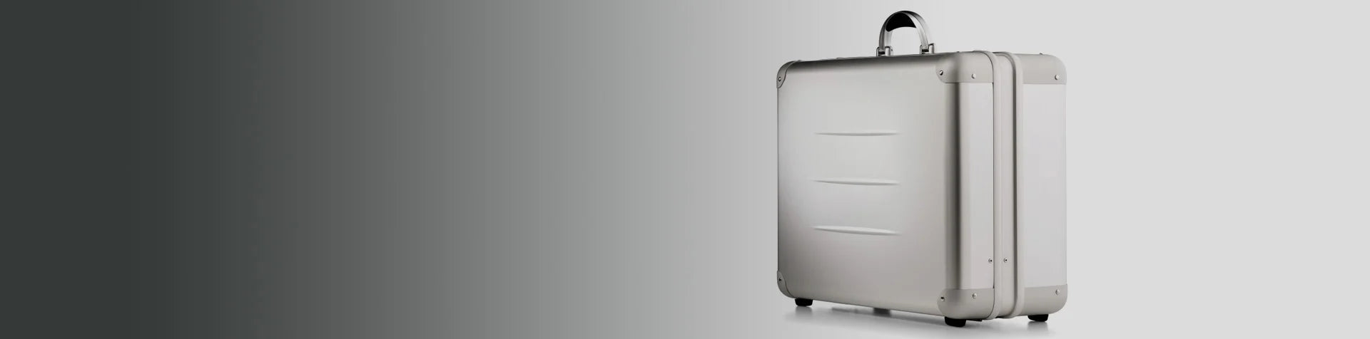 A silver hard-shell suitcase with a black handle is positioned on a light grey background, facing right.
