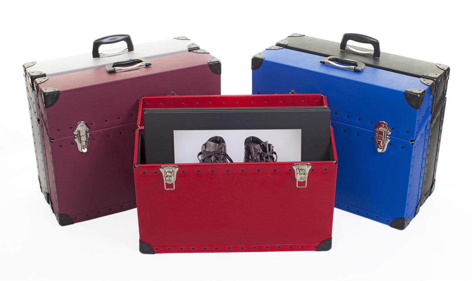 Three sturdy, rectangular carrying cases—one red, one blue, one burgundy—stand upright, with the red case open revealing artwork or prints inside.