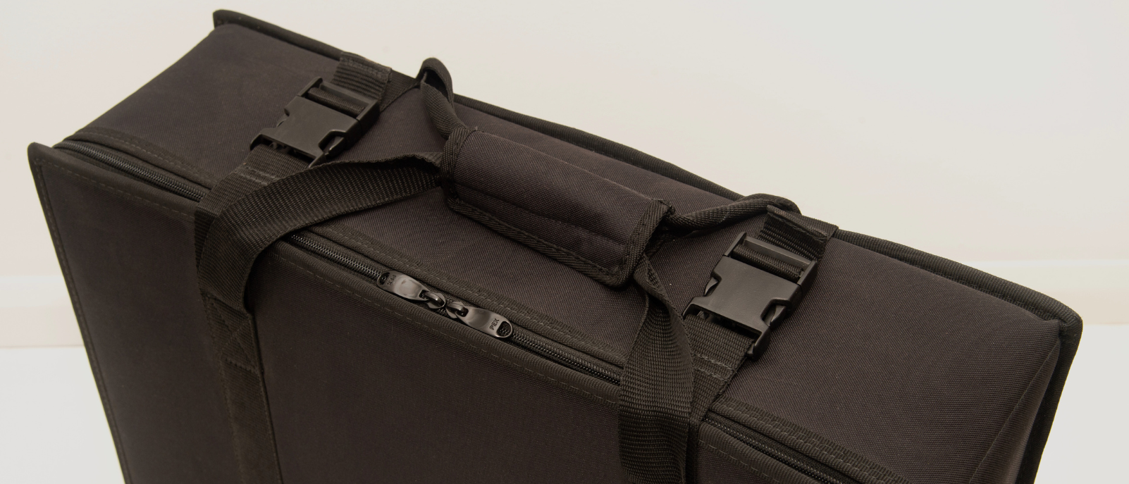 A close-up view of a black soft-sided carrying case with a handle, zipper closure, and adjustable straps against a plain background.