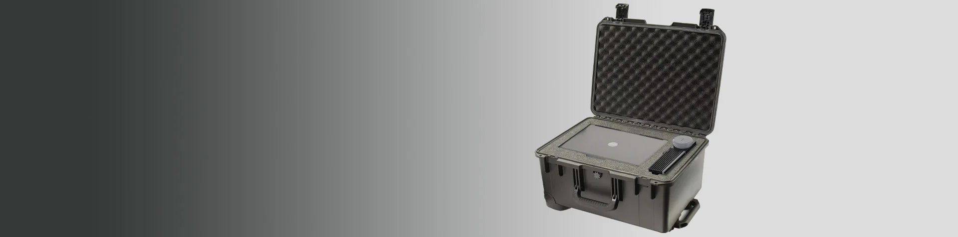 A black, rugged protective case with an open lid reveals a control panel and a rotary dial inside, set against a gradient gray background.