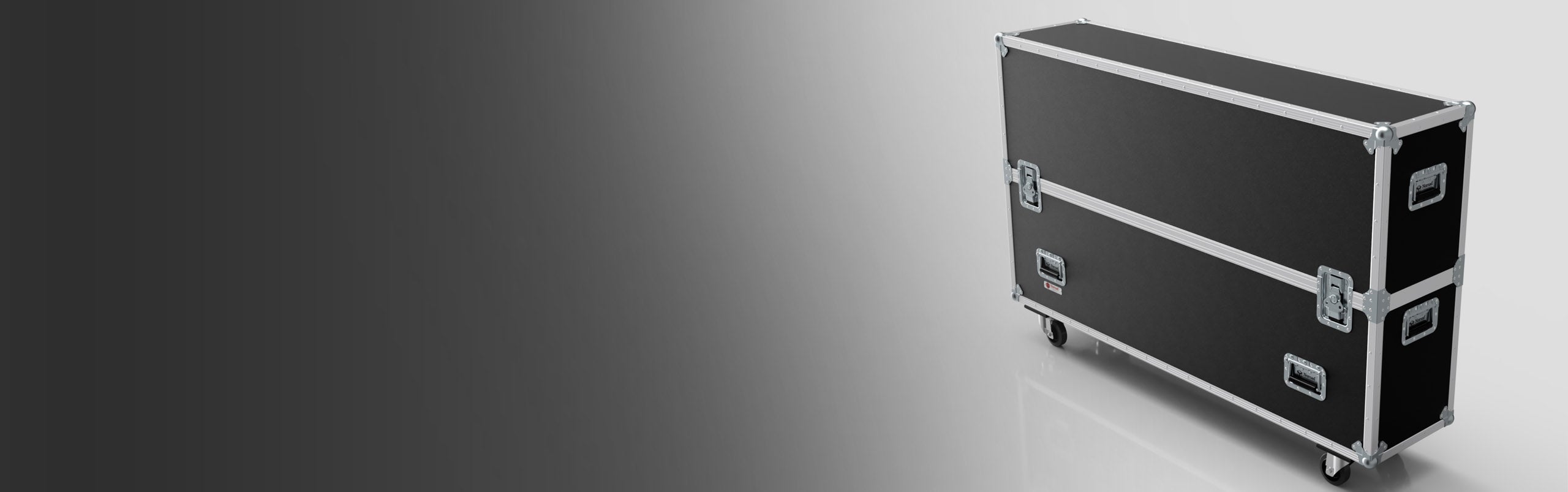 A large black rectangular equipment case with metal edges, latches, handles, and caster wheels on a white and gray gradient background.
