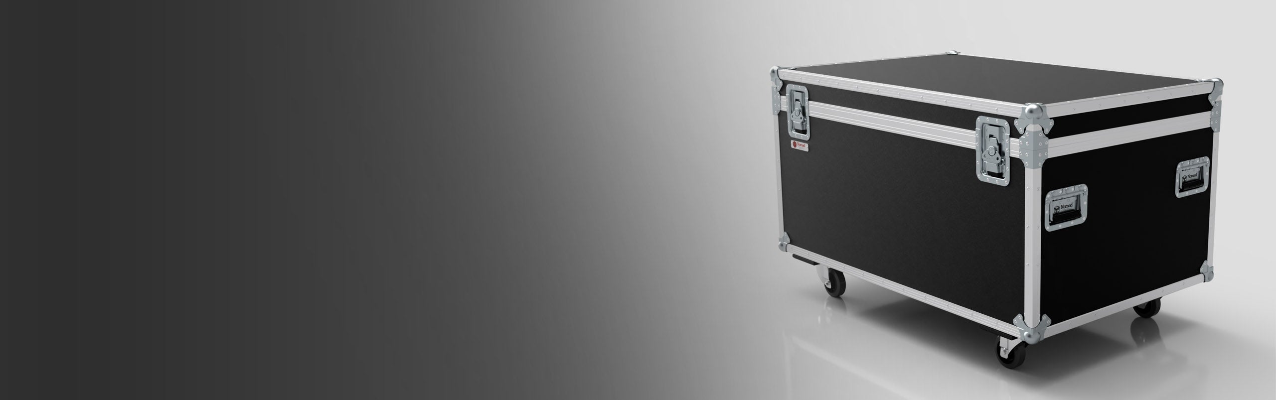 A large black and silver flight case with metal edges and corners, mounted on four wheels, positioned on a reflective floor against a gradient background.