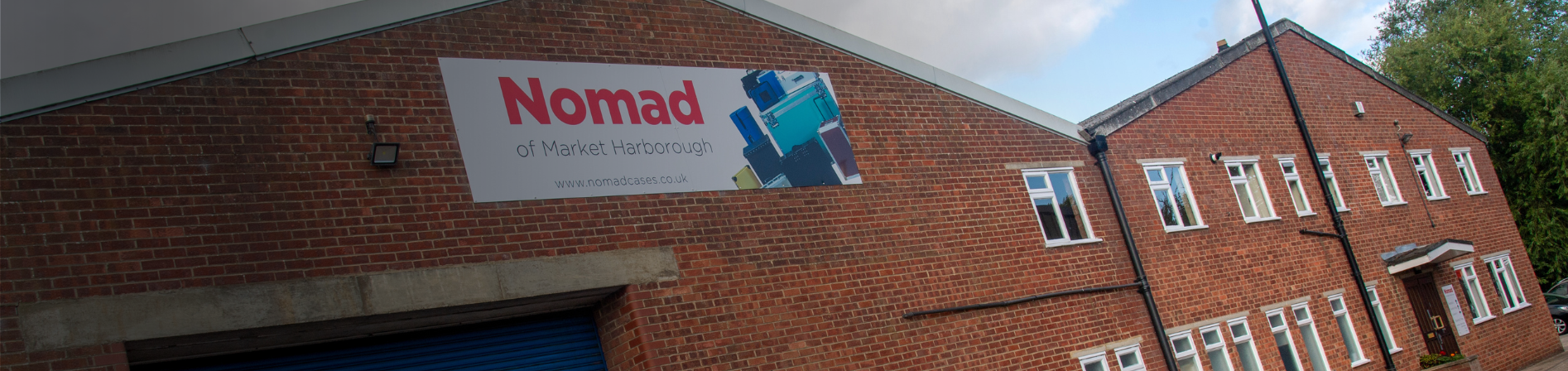 A brick commercial building with a large sign reading Nomad of Market Harborough above a blue roller door and several windows.