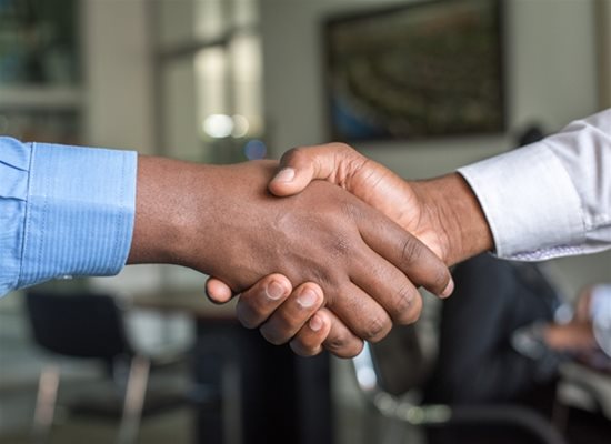Two people wearing dress shirts shaking hands in an office setting.