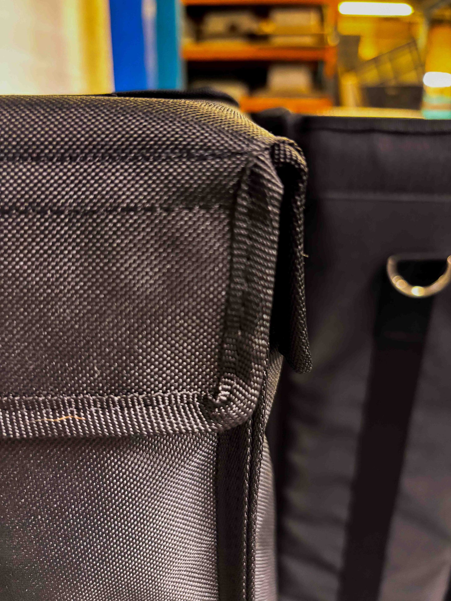 Close-up of two black textured fabric DB Audio D8 Sub Woofer Custom Covers with flap covers for road-ready protection. Shot indoors, shelves and lights blurred in the background. Perfect for your subwoofer.