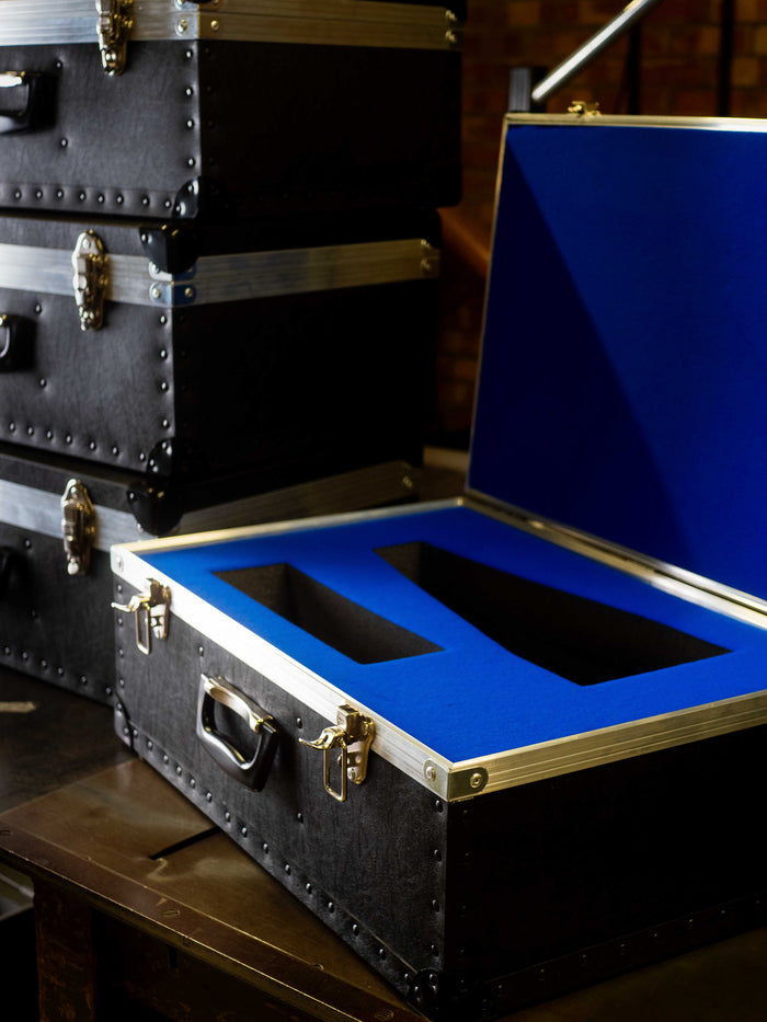 A stack of black cases sits on a table, with one open to reveal blue foam inserts with two cutouts for securely holding items.