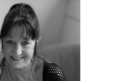 Black and white photo of a woman with dark hair tied back, wearing a light shirt and a dark sweater, smiling at the camera.