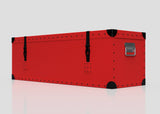The Football Storage Poly Case (Medium) is a rectangular red trunk with black corner protectors, rivet details, two black webbing straps with side-release buckles, and a silver handle on one end, shown against a plain background.